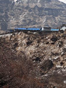 A mountainous landscape featuring rugged terrain and a few buildings with blue roofs situated on a ridge.