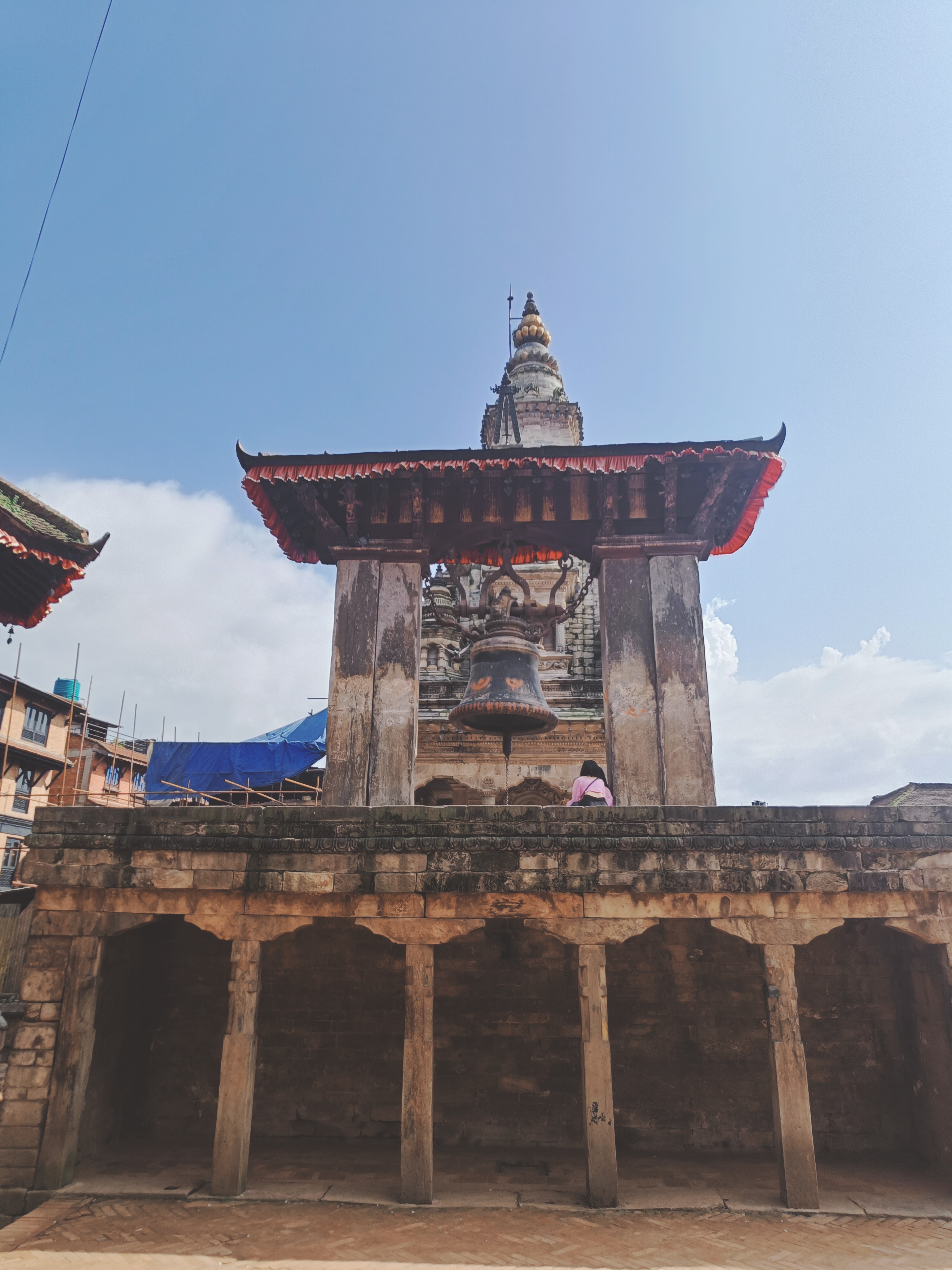 A traditional architectural structure featuring a large bell hanging beneath a roofed pavilion.