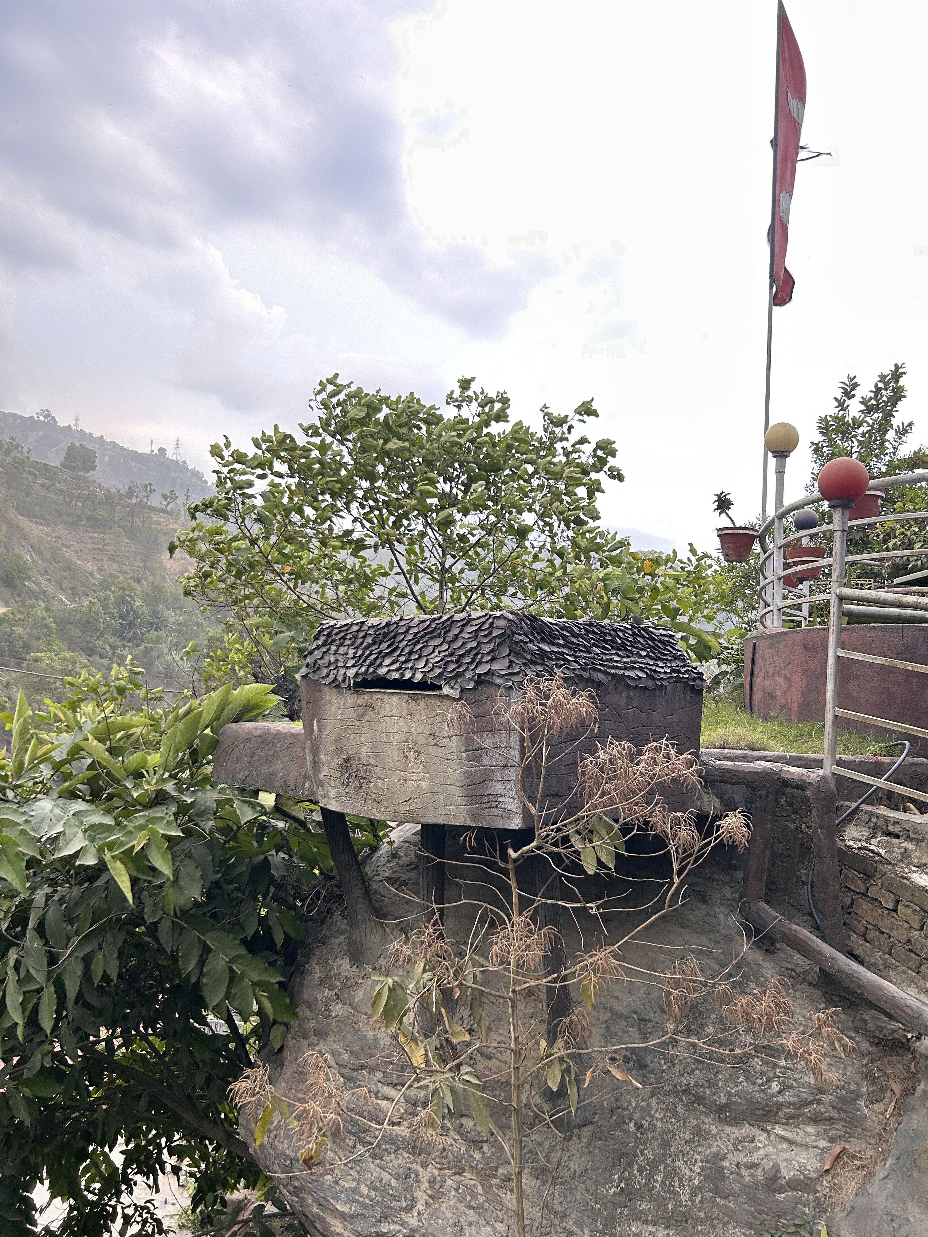 A rustic wooden structure with a thatched roof is perched on a rock, surrounded by lush greenery.